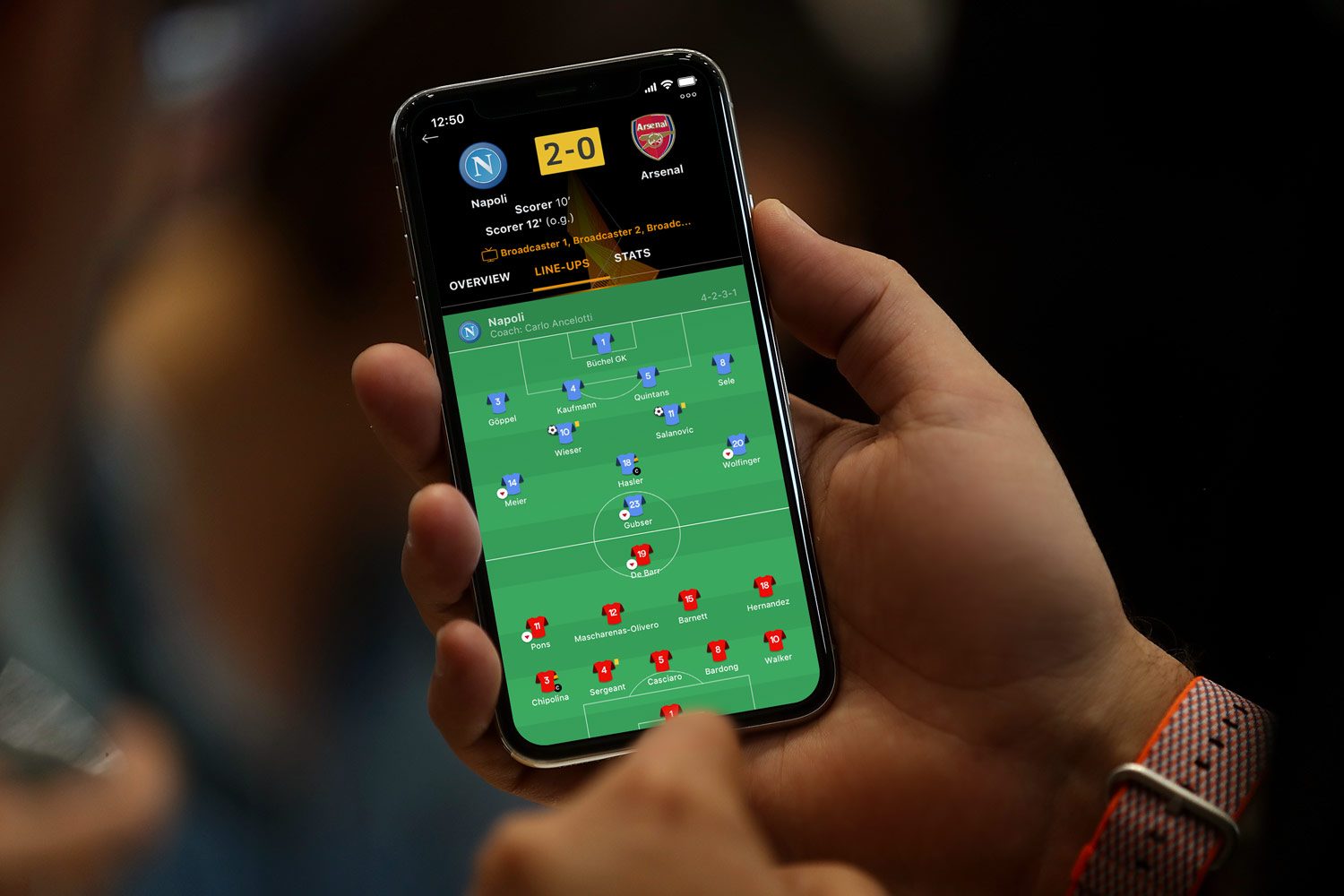 UEFA Champions League Match Center app showing Napoli 2-0 Arsenal with line-ups, held in hand